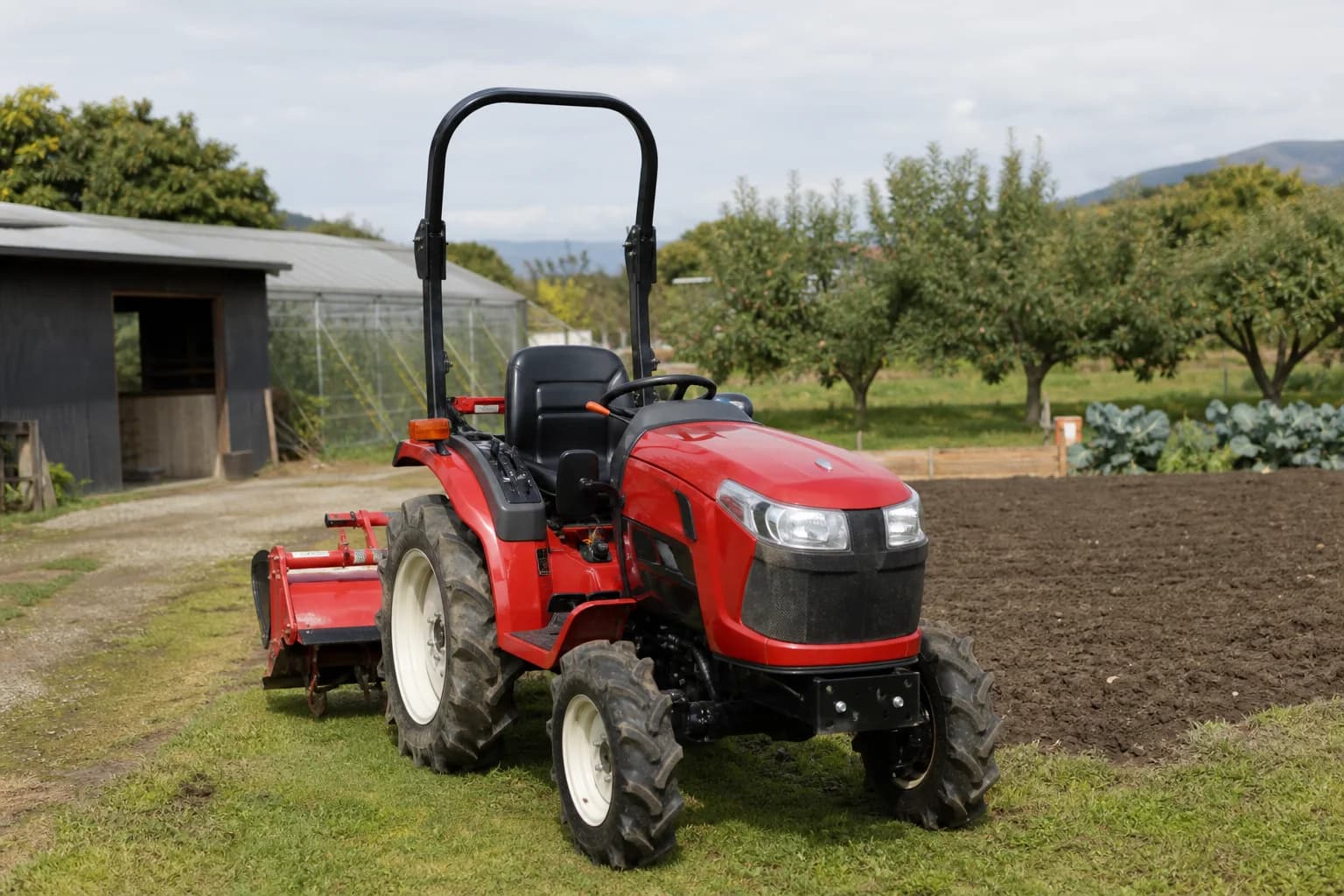 Kompaktný japonský malotraktor s pripojeným náradím na okraji záhrady a malej farmy.