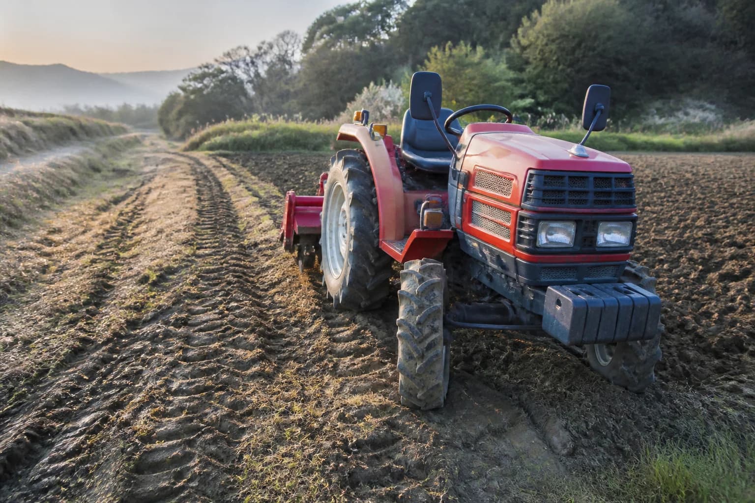 Malotraktor s pripojeným náradím stojí na nerovnom poli s vytočenými prednými kolesami.